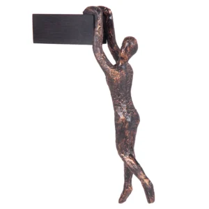 Escultura de resina na fisionomia de um homem, segurando com as mãos a base também de resina com abertura para ser pendurada na parede. Adorno de acabamento rústico criado para ser exposto na parede com a escultura voltada para frente como se estivesse pendurado. Desenvolvido e fabricado nacionalmente pela Modali Design.
