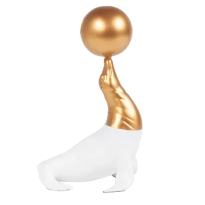Escultura feita de resina em tonalidade branca e dourada, com desenho artístico de uma foca com uma bola dourada. Adorno de acabamento liso criado para ser exposto sobre mesas, aparadores, estantes e prateleiras. Desenvolvido e fabricado nacionalmente pela Modali Design.