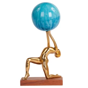 Escultura feita de alumínio em tonalidade dourada e com base de madeira natural, com desenho artístico de corpo agachado com as mãos para cima segurando o globo do mapa mundi feito em resina colorida. Adorno de acabamento liso criado para ser exposto sobre mesas, aparadores, estantes e prateleiras. Desenvolvido e fabricado nacionalmente pela Modali Design.