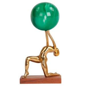 Escultura feita de alumínio em tonalidade dourada e com base de madeira natural, com desenho artístico de corpo agachado com as mãos para cima segurando o globo do mapa mundi feito em resina colorida. Adorno de acabamento liso criado para ser exposto sobre mesas, aparadores, estantes e prateleiras. Desenvolvido e fabricado nacionalmente pela Modali Design.