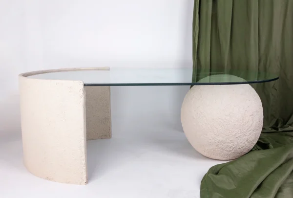 Mesa de centro feita em resina com tonalidade bege clara e com aspecto rústico e tampo de vidro incolor apoiado sobre base em formato de esfera em resina. Desenvolvido e fabricado nacionalmente pela Modali Design.